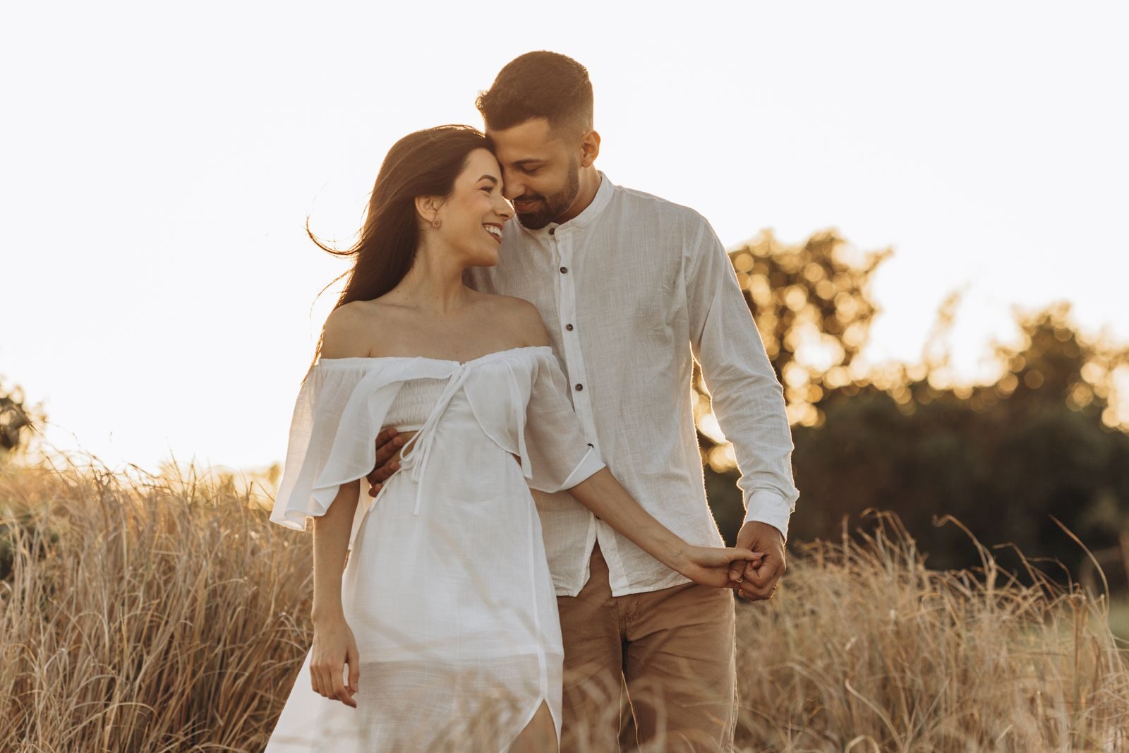 Young couple embracing in a sunny rural field, expressing love and happiness.
